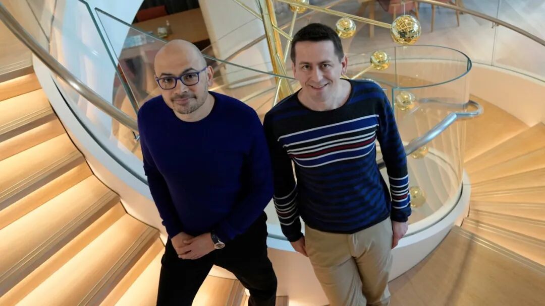 John Jumper, left, and Demis Hassabis stand together on a spiral staircase at the Google DeepMind offices.