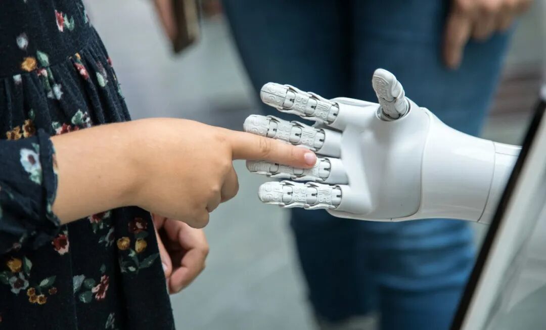 A child touching the finger of a white robotic hand