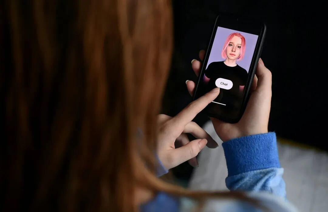 Person holds a smartphone showing a pink-haired digital avatar while tapping a button on the screen.